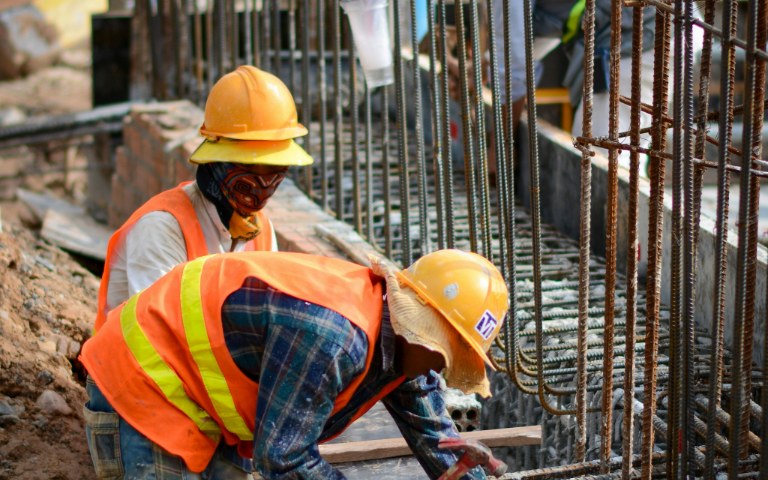 Two construction workers in hard hats tying rebar together on an active jobsite